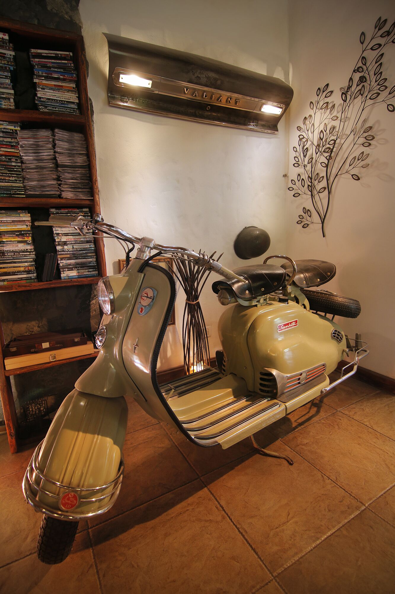 A vintage scooter in a room with a bookshelf filled with DVDs and a wall decoration.