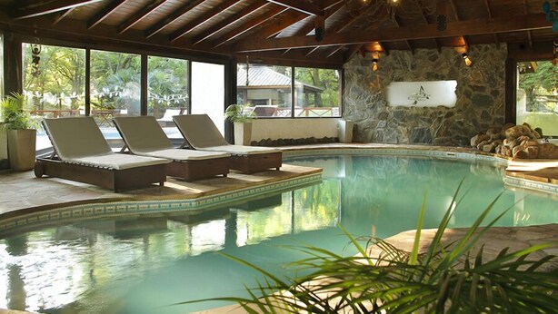 A pool area with lounge chairs, a stone wall, and a view of the outdoors. - Posada del Sauce (Villa General Belgrano)