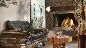 A cozy living room with a leather sofa, a vintage car model, a wooden coffee table with books, a fireplace, and decorative plants. - Posada del Sauce (Villa General Belgrano)