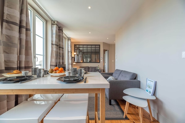 A modern living room with a grey sofa, a white coffee table, and a dining area with a white table and chairs.