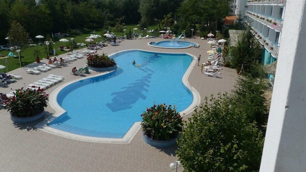 Una piscina con sillones de descanso y sombrillas, rodeada de vegetación y un edificio de hotel.