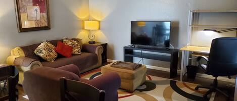 Una sala de estar con un sofá, una televisión, un escritorio y una silla.