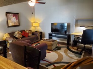 A living room with a sofa, a TV, a desk, and a chair.