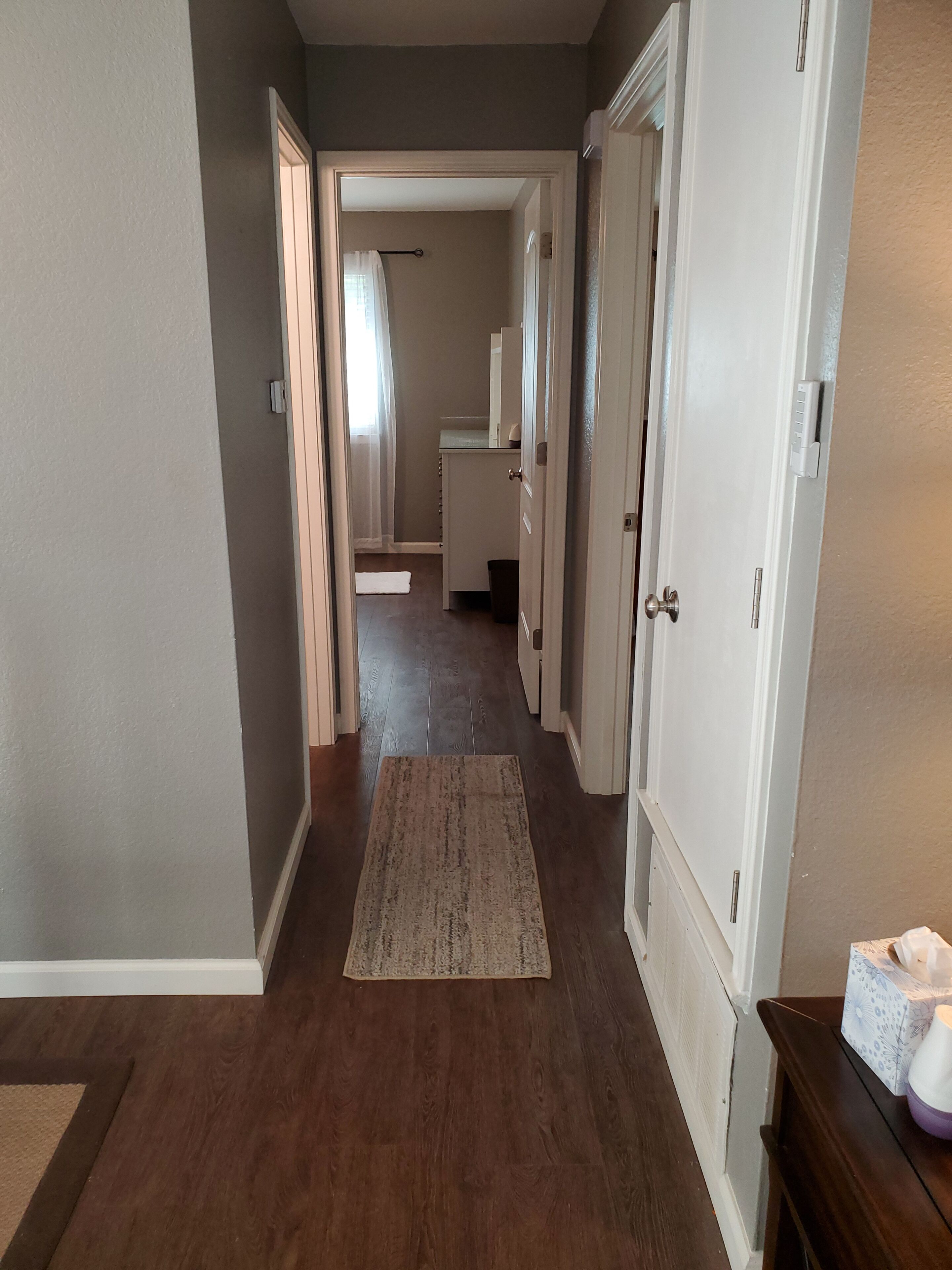 A hallway with wooden flooring, a rug, and white doors leading to other rooms.