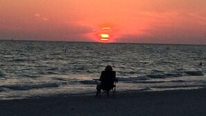 A person sitting on a beach chair facing the ocean during sunset.