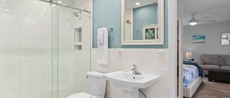 A modern bathroom with a glass-enclosed shower, a white toilet, and a pedestal sink.