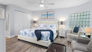 A bedroom with a bed, bedside tables, a chair, a ceiling fan, and a window with a view.