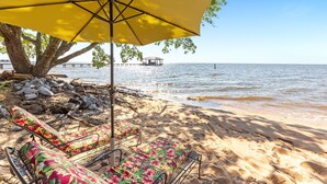 Ein Strand mit Liegestühlen und einem gelben Sonnenschirm, im Hintergrund ein Steg und ein klarer Himmel.