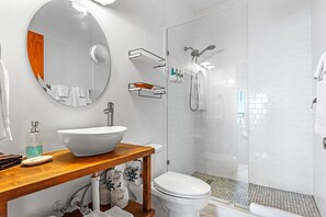 A modern bathroom with a large oval mirror, a white sink, a toilet, and a glass-enclosed shower area.