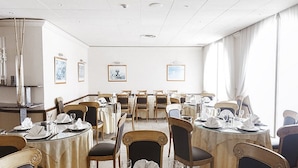 Een vergaderruimte met ronde tafels, stoelen en ingelijste foto's aan de wanden.