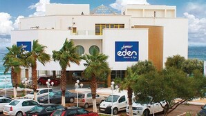 Een modern gebouw met een opvallend bord waarop 'eden Resort & Spa' staat, met een helder uitzicht op de oceaan en een parkeerplaats met meerdere auto's.