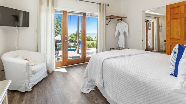 Un dormitorio con una cama grande, un sillón blanco, un televisor y vistas al exterior.
