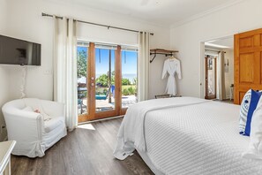 Un dormitorio con una cama grande, un sillón blanco, un televisor y vistas al exterior.