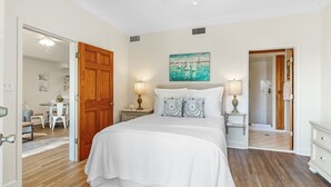 Un dormitorio con una cama grande, dos mesitas de noche con lámparas, un cuadro en la pared y una puerta de madera.