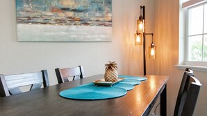 A dining area with a wooden table, blue placemats, a pineapple centerpiece, and a painting on the wall.