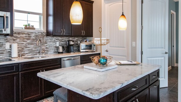 A modern kitchen with dark wood cabinets, a marble countertop, a built-in microwave, and pendant lighting.