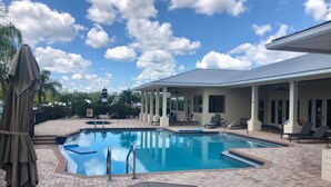 A swimming pool with a tiled deck, lounge chairs, and a covered patio area.