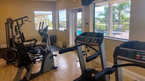 A gym with cardio machines, weight equipment, and large windows offering views of a pool and palm trees.