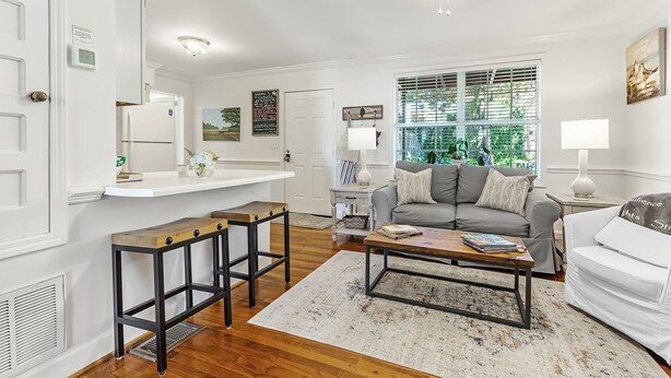 A modern living room with a gray sofa, a coffee table, and a kitchen area with a white refrigerator. - Magnolia at Jubilee Suites Bed & Breakfast. 1K/1B. (Fairhope)