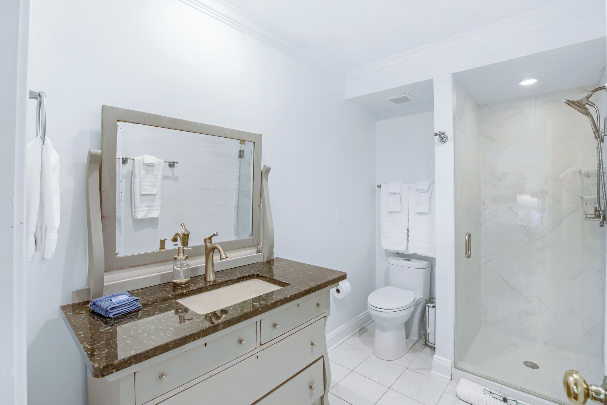 Et stilfuldt badeværelse med et stort spejl, en vask med marmor bordplade, toilet og bruseområde med glasvægge.