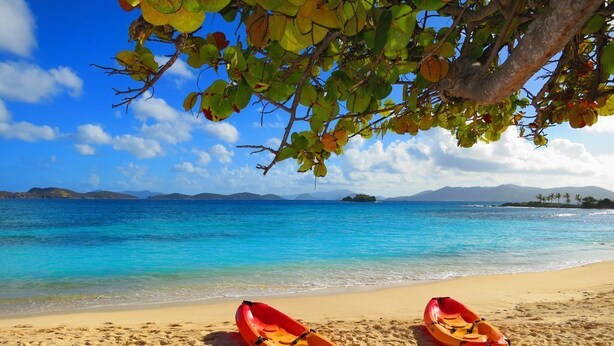 Deux kayaks rouges sur une plage de sable, avec une eau d’un bleu limpide et des îles qui se dessinent à l’horizon.