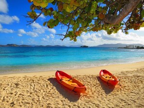 Two red kayaks on a sandy beach with clear blue water and distant islands.