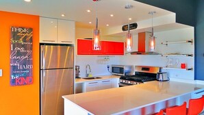 Une cuisine moderne dotée d’un îlot central, d’appareils électroménagers en acier inoxydable et de touches de couleur rouge.