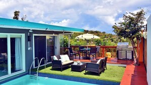 Un espace piscine extérieur moderne doté d’un patio fermé par des baies vitrées, d’un barbecue et de coins salon extérieurs.