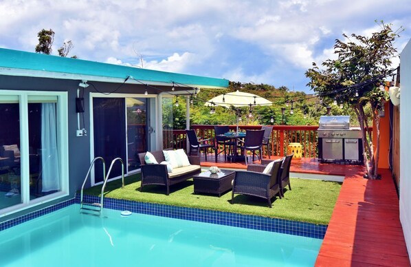 A modern outdoor pool area with a glass-enclosed patio, a barbecue setup, and outdoor seating.