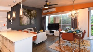Une cuisine moderne dotée d’un îlot central, d’un coin repas avec des chaises orange et d’une grande fenêtre donnant sur un paysage verdoyant.