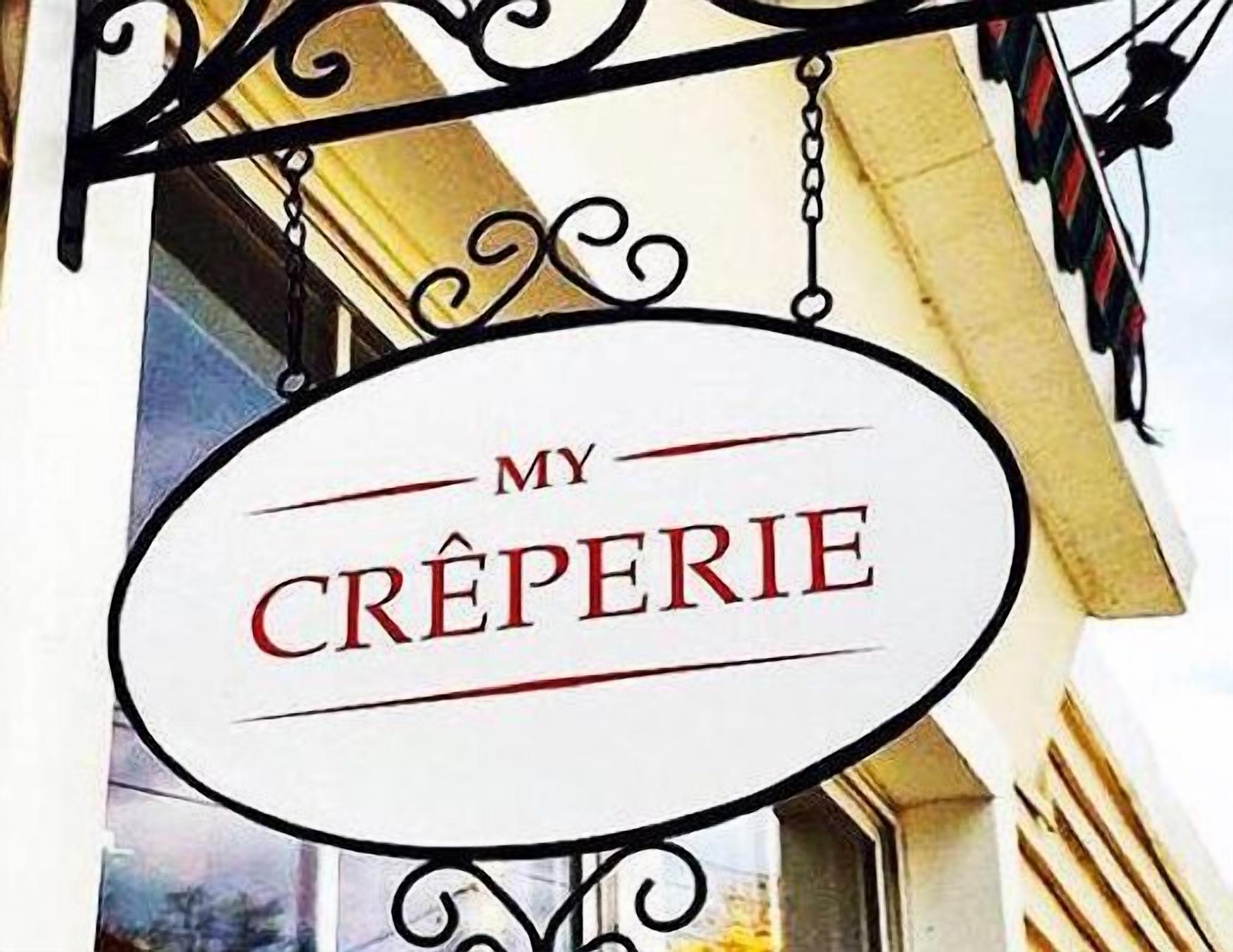 A sign with the text "MY CREPERIE" hanging from a metal structure.