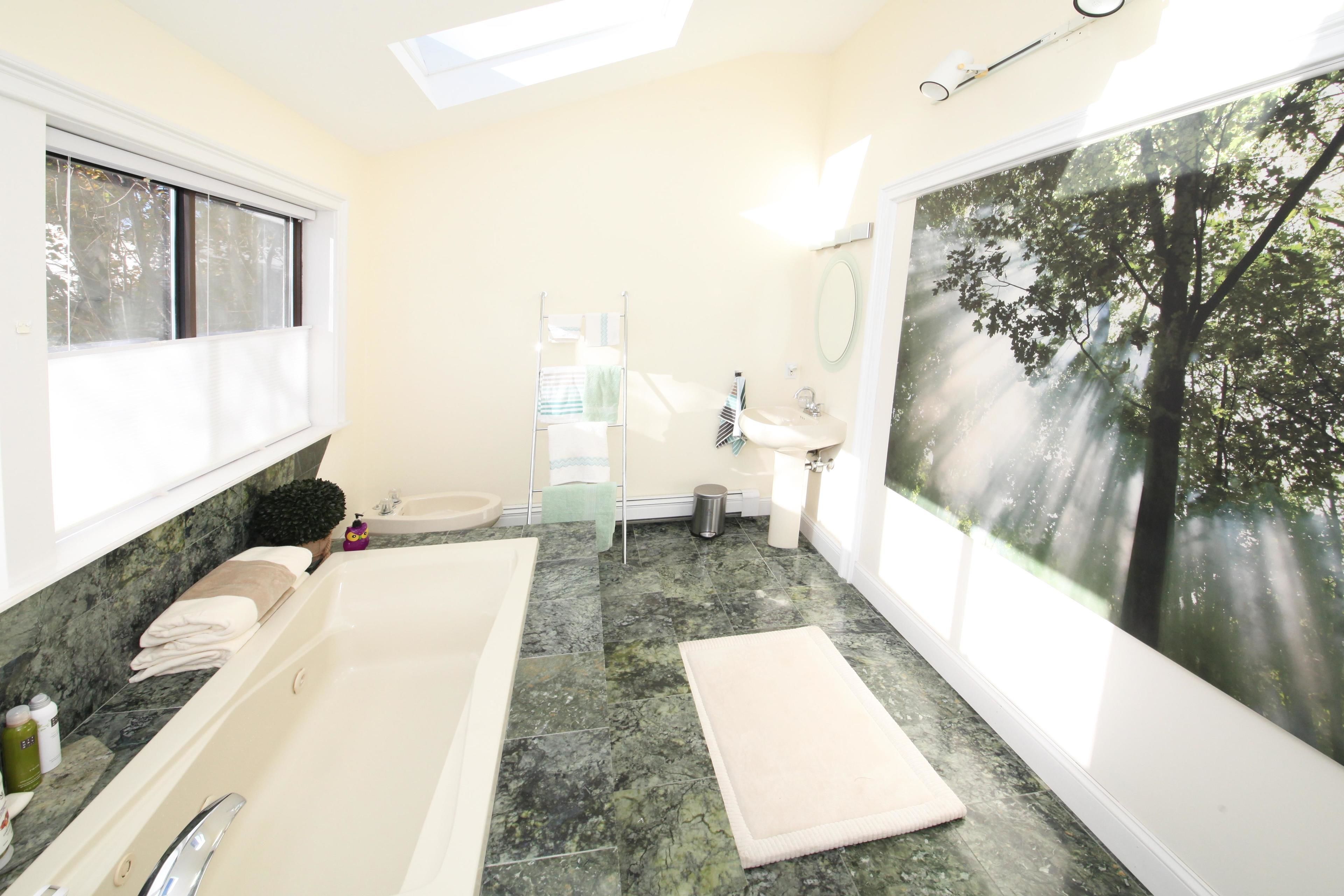 Une salle de bain avec une baignoire, un lavabo et une grande fenêtre donnant sur un arbre.