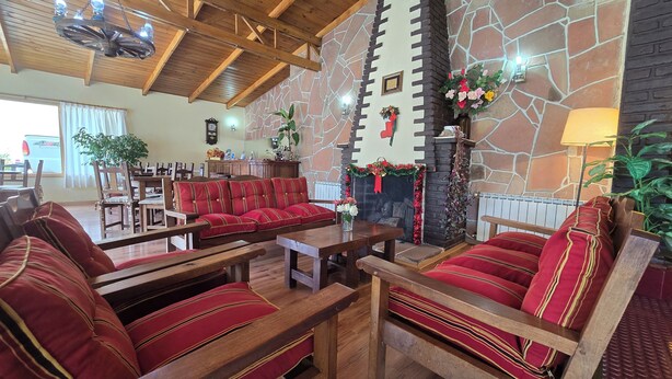 A cozy lobby with wooden furniture, a stone wall, and a fireplace decorated with festive garlands. - Hotel Upsala (El Calafate)
