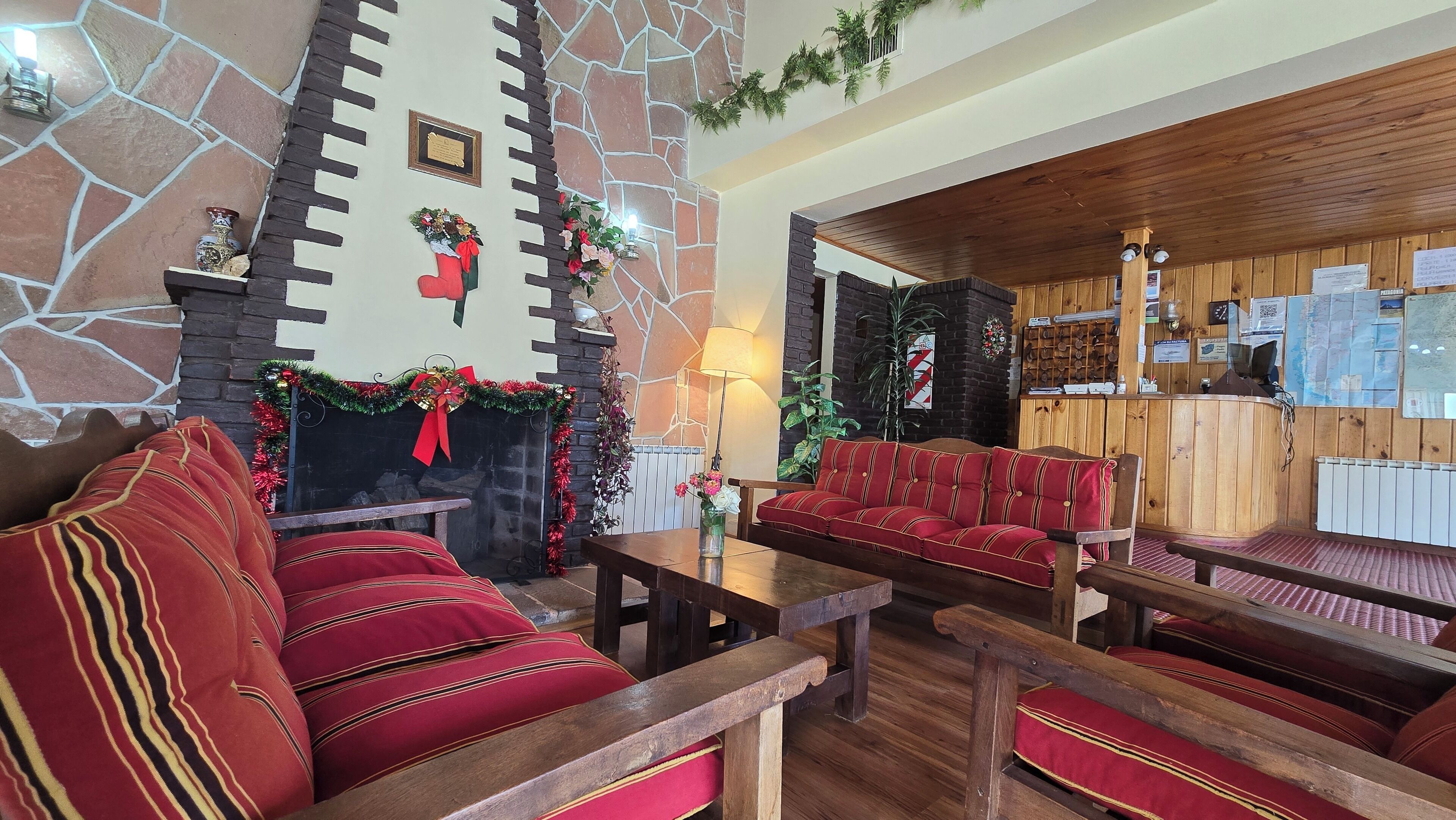 Un'accogliente hall con pareti in pietra, un camino, sedute imbottite rosse e una reception.