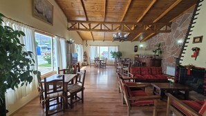 A spacious room with wooden floors, a high ceiling with exposed beams, a fireplace, and a dining area with wooden furniture. - Hotel Upsala (El Calafate)
