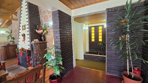 A reception area with a wooden reception desk, a stone wall with a fireplace, and potted plants. - Hotel Upsala (El Calafate)