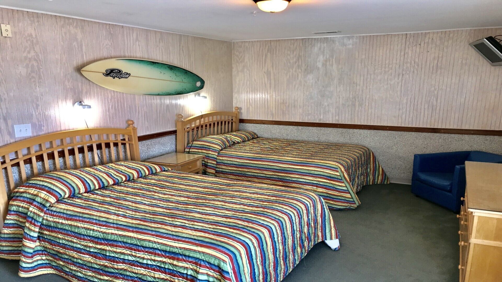 A room with two beds, a small table, and a surfboard on the wall.