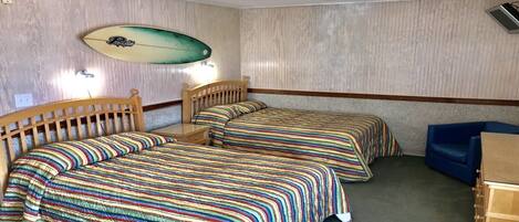 A room with two beds, a small table, and a surfboard on the wall.