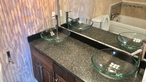 A bathroom with a glass bowl sink, a toilet, and a bathtub.