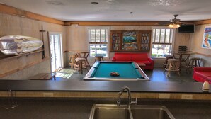 A pool table in a room with a red sofa, wooden chairs, and a bookshelf.