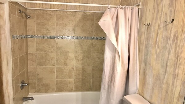 A shower area with beige tiles, a showerhead, and a curtain.