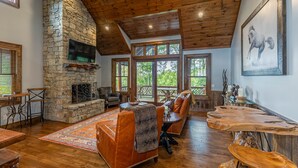 A spacious living room with a stone fireplace, wooden ceiling, and large windows. - Prancing Horse at Eagles Nest - hot tub, great view, resort amenities, summer concerts! (Banner Elk)