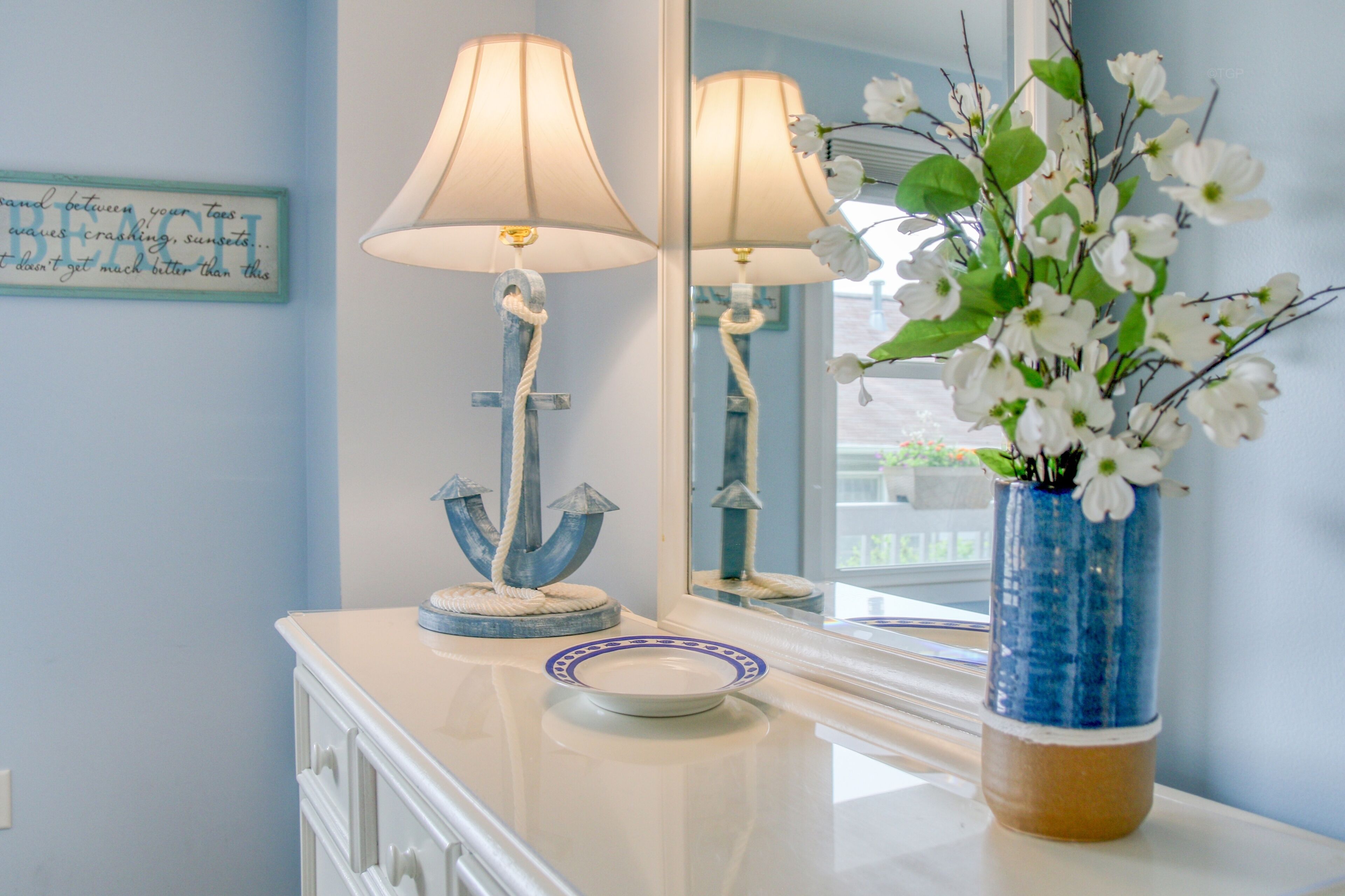 A bathroom vanity with a mirror, two lamps, a vase with flowers, and a decorative plate.