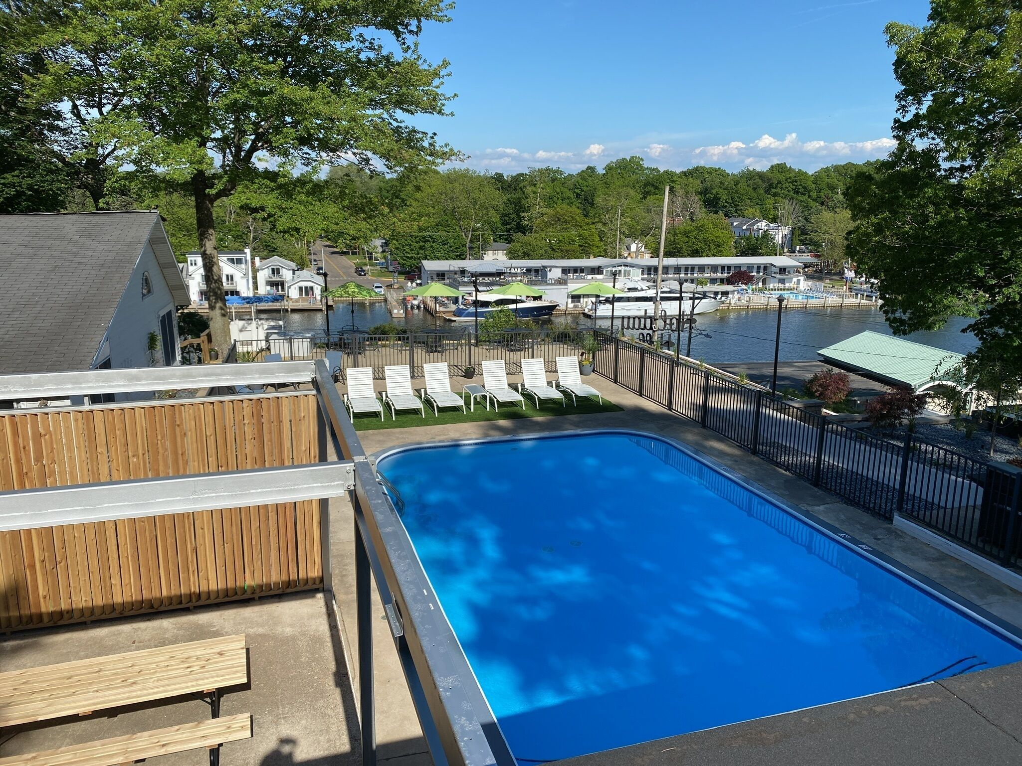 A swimming pool with lounge chairs, a wooden deck, and a view of a marina with boats.