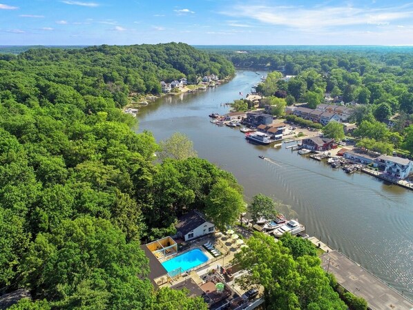 Luchtbeeld van een stad aan de rivier met een zwembad, aangemeerde boten en woongebouwen.