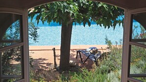 Vista dalla finestra su una piscina, con un albero e una sedia.