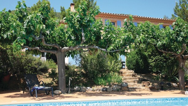 Un'area piscina con una piscina blu cristallina, circondata da alberi e una scala in pietra che conduce a un edificio con tetto in tegole.
