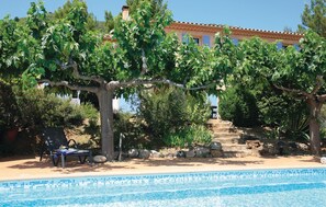 Un espace piscine avec une eau d’un bleu limpide, entouré d’arbres et agrémenté d’un escalier en pierre menant à un bâtiment doté d’un toit en tuiles.