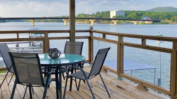 A wooden deck with a table and chairs overlooking a river with bridges and buildings in the background. - The Overlook at Lake Hamilton - Contemporary Design, Private Deck & Boat Slip! (Hot Springs)