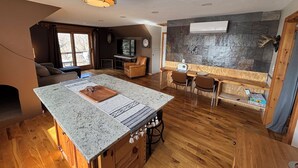 A cozy living area with a wooden floor, a central island with a kitchen counter, a television, and a stone wall.